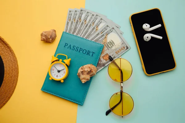 Koncepcja wakacji. Okulary przeciwsłoneczne, smartfon, kapelusz i paszport z banknotami na niebiesko żółtym tle — Zdjęcie stockowe