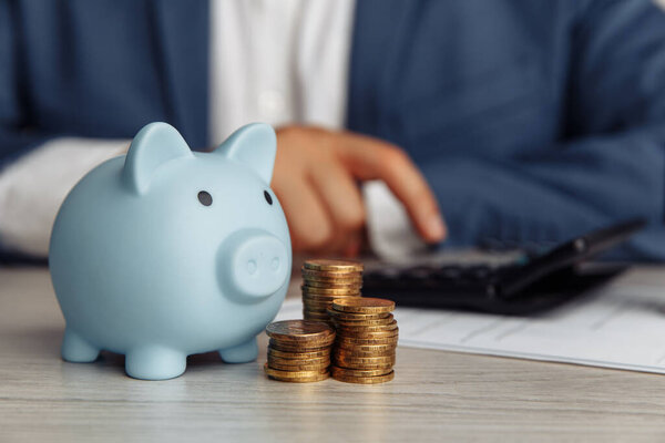 Man is counting profit on a calculator, piggy bank and coins on wooden desk in office. Economy and management financial concept