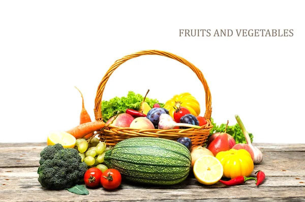 Basket with vegetables and fruits on wooden table, on white background.Useful vitamins.