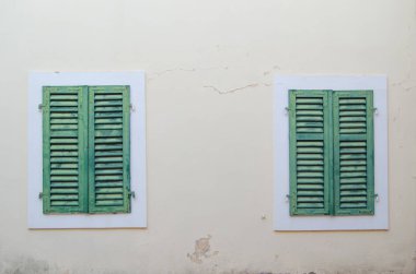 İki eski Windows ile bej duvara karşı yeşil panjurlar kapalı.
