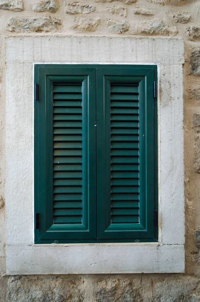 One vintage window is covered with green shutters on the background of a beige wall.