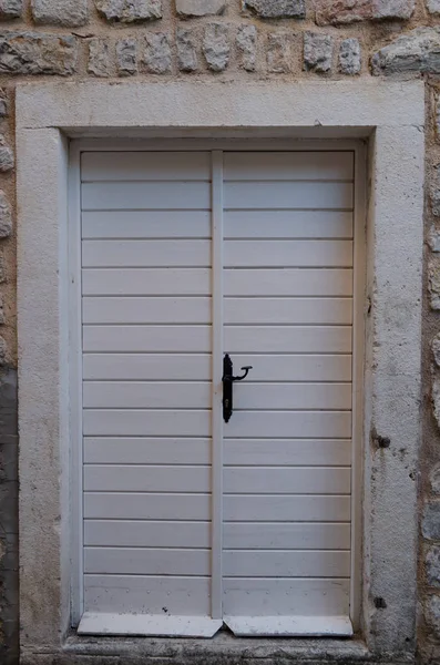 Old wooden, white the door closed on iron bolt.On metal canopies.