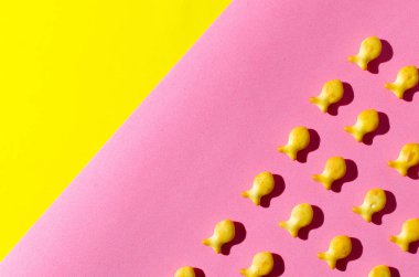 Pembe ve sarı zemin üzerine bir balık şeklinde kurabiyeler. Parlak gün ışığında gölgeler.