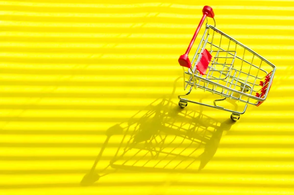 明るい日光と影と黄色の背景にショッピングカート. — ストック写真