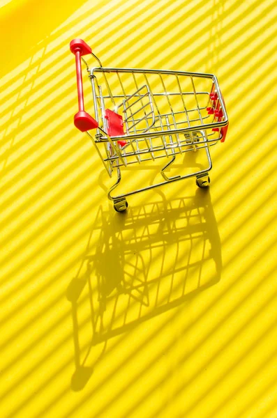 明るい日光と影と黄色の背景にショッピングカート. — ストック写真