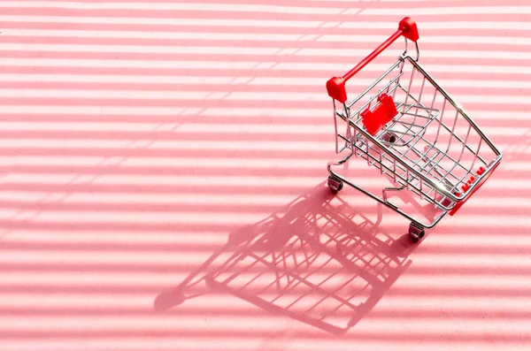 明るい日光と影とピンクの背景にショッピングカート. — ストック写真