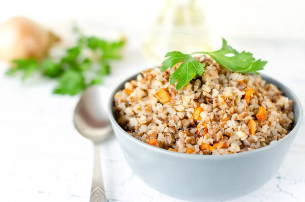 Mavi tabakta havuç ve maydanoz ile karabuğday lapası. Altın soğan ve yeşil maydanoz arka planda.