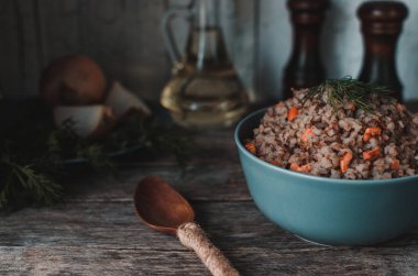 Eski bir rustik, ahşap arka plan üzerinde havuç ile karabuğday lapası. Çatal bıçak, yağ şişesi, dereotu, biber ve tuzluk, soğan.