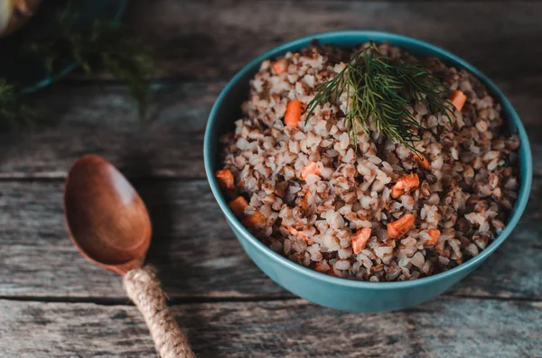 Eski bir rustik, ahşap arka plan üzerinde havuç ile karabuğday lapası. Çatal bıçak, yağ şişesi, dereotu, biber ve tuzluk, soğan.
