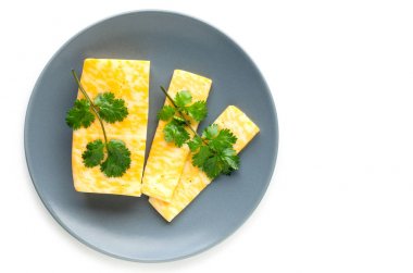 Dilimlenmiş maydanoz peyniri beyaz bir arka plan üzerinde gri bir tabak üzerine yayıldı.