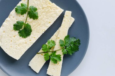 Dilimlenmiş maydanoz peyniri beyaz bir arka plan üzerinde gri bir tabak üzerine yayıldı.