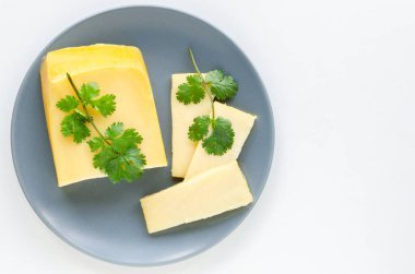 Dilimlenmiş maydanoz peyniri beyaz bir arka plan üzerinde gri bir tabak üzerine yayıldı.