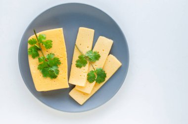 Dilimlenmiş maydanoz peyniri beyaz bir arka plan üzerinde gri bir tabak üzerine yayıldı.