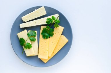 Dilimlenmiş maydanoz peyniri beyaz bir arka plan üzerinde gri bir tabak üzerine yayıldı.