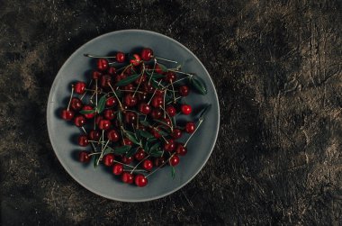Eski bir beton, rustik arka plan üzerinde gri bir tabak içinde parlak, kırmızı, olgun kiraz berry.