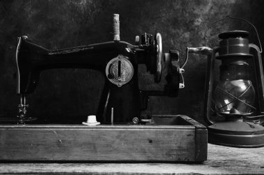 Eski, eski, antika dikiş makinesi ve soyut bir duvarın karanlık arka planında bir gaz lambası.