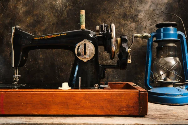 Old, retro, vintage sewing machine and a kerosene lamp on a dark background of an abstract wall