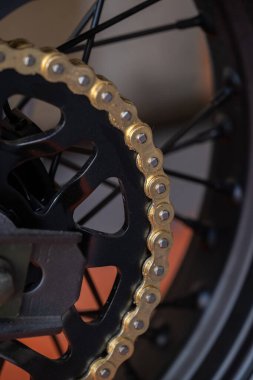 Bisiklet zinciri ve çıkıntıya yakın çekim. Zincir altın ve çıkıntı siyah. Karmaşık detaylar ve dokular sergiliyor..