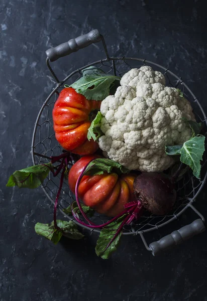 Fresh organic vegetables - cauliflower, tomatoes, beets in vintage metal basket on dark background, top view