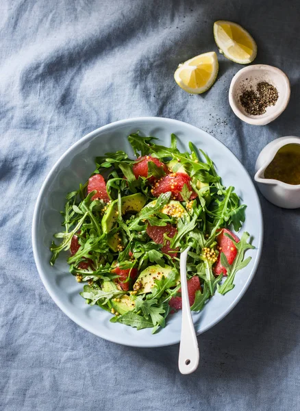 Avocado, grapefruit, rocket salad with mustard olive oil salad dressing on blue background, top view. Vegetarian diet food concept