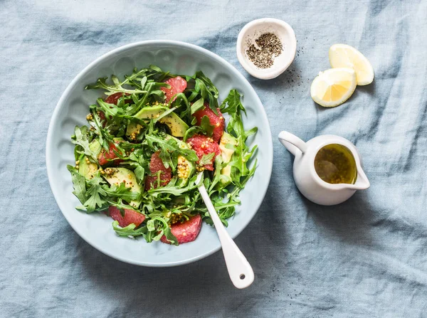 Avocado, grapefruit, rocket salad with mustard olive oil salad dressing on blue background, top view. Vegetarian diet food concept