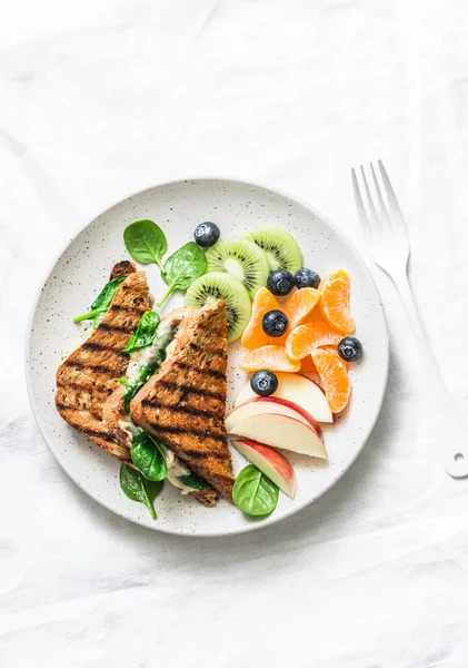 Tuna, spinach, mozzarella hot toast and fresh fruit - delicious healthy breakfast, brunch, snack on a light background, top view. Copy space