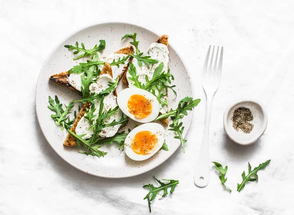 Easter brunch. Delicious breakfast, brunch or snack - cream cheese toast, arugula salad and soft boiled egg on a light background, top view