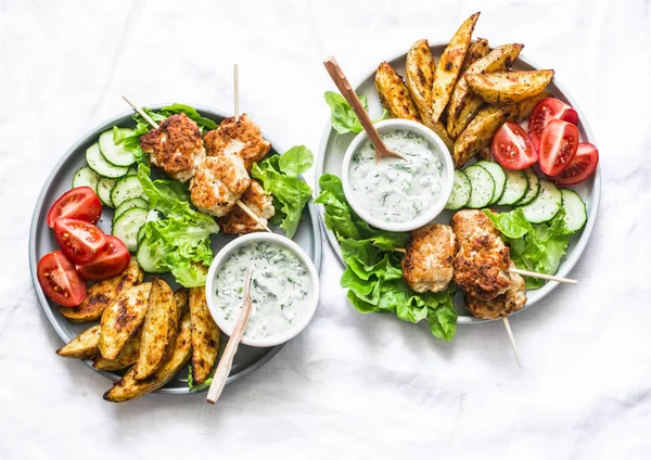 Big lunch plate - fish kebabs, roasted lemon potatoes, tzatziki sauce and fresh vegetables on a light background, top view — Stock Image Big Lunch Plate Fish Kebabs Roasted Lemon Potatoes Tzatziki Sauce Royalty Free Stock Photos