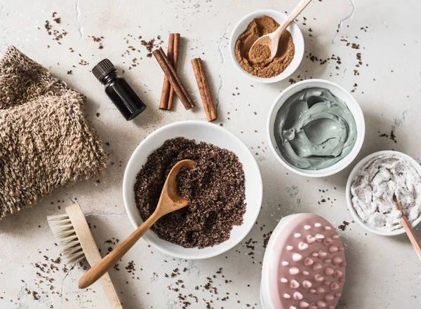 Home anti-cellulite products - coffee scrub, cosmetic clay, essential orange oil, hand anti-cellulite massager, nut scrub, cinnamon, natural loofah on a light background, top view. Beautiful healthy body concept