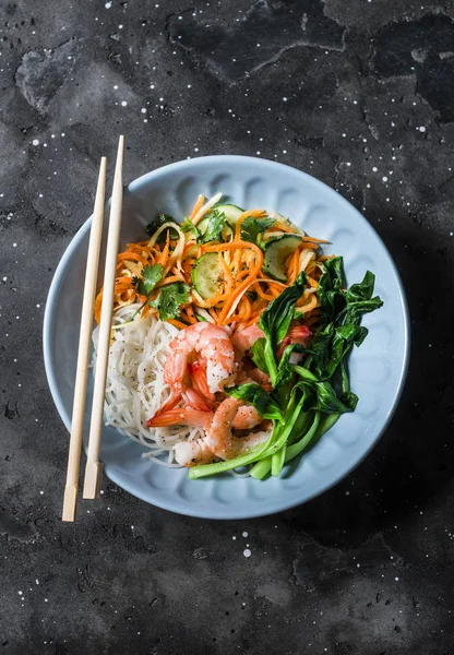 Asian food bowl - rice noodles, shrimp, cabbage bok choy and quickly pickled vegetables carrots, cucumbers, daikon salad on a dark background, top view — Stock Image Asian Food Bowl Rice Noodles Shrimp Cabbage Bok Choy Quickly Royalty Free Stock Photos