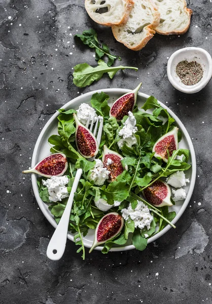 Figs, goat cheese, arugula salad on dark background, top view