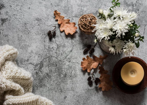 Cozy autumn background. Candle, autumn flowers, knitted blanket, dry leaves on a gray background, top view