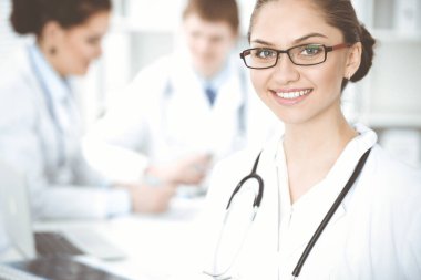 Mutlu gülümseyen kadın doktor tıbbi personelle toplantıda oturup kameraya bakıyor. Tıp konsepti
