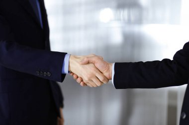 İş adamları el sıkışıyor, yakın plan. Modern bir ofiste duran bir grup tanınmamış iş adamı. Takım çalışması, ortaklık ve el sıkışma kavramı