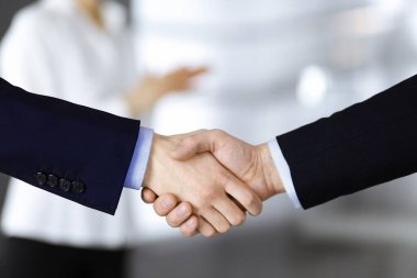 İş adamları toplantıda ya da pazarlıkta el sıkışıyor, yakın plan. Bir grup tanınmamış iş adamı ve modern bir ofiste duran bir kadın. Takım çalışması, ortaklık ve el sıkışma kavramı