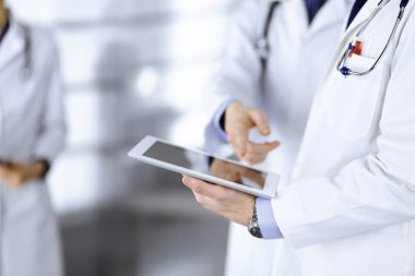 Bilinmeyen bir grup doktor hastane ofisinde dururken bazı tıbbi isim kayıtlarını kontrol etmek için bir bilgisayar tableti kullanıyor. Doktorlar hastaları muayene etmeye ve yardım etmeye hazır. Tıbbi yardım, sigorta