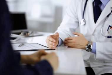 Bir doktor, hastanedeki dolapta birlikte otururken hastasıyla konuşuyor. Doktor ilaç kayıtlarını doldurmak için pano kullanıyor. Mükemmel tıbbi hizmet...