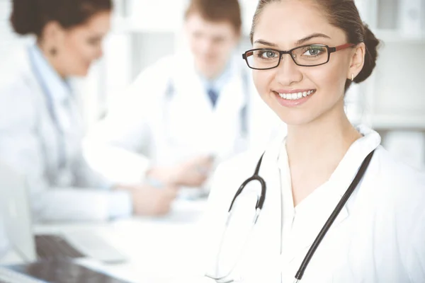 Feliz mujer-médico sonriente sentado y mirando a la cámara en la reunión con el personal médico. Concepto de medicina — Foto de Stock