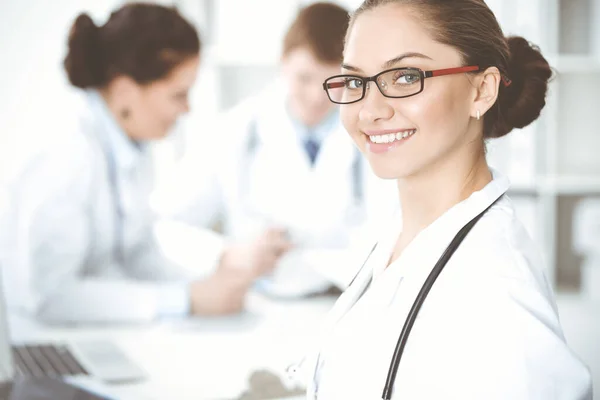 Szczęśliwa uśmiechnięta kobieta-lekarz siedząca i patrząca przed kamerą na spotkanie z personelem medycznym. Koncepcja medycyny — Zdjęcie stockowe