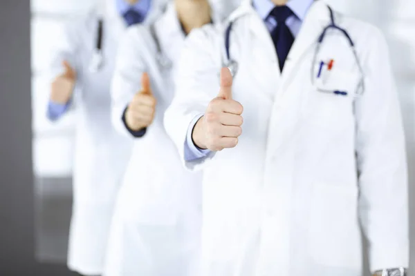 Group of unknown doctors stand as a team with thumbs up in a hospital office. Physicians ready to examine and help patients. Medical help, insurance in health care, best desease treatment and medicine — Stock Photo, Image