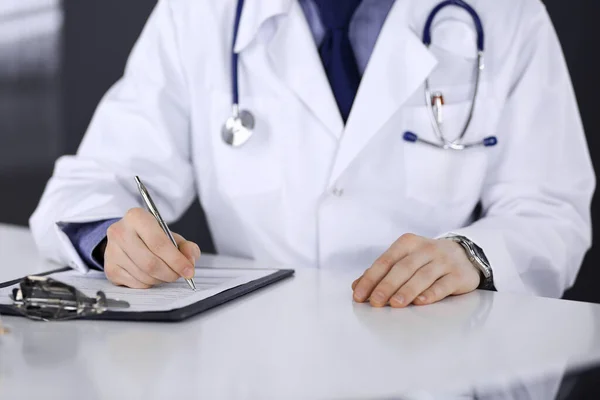 Médico desconhecido sentado e trabalhando com prancheta de registro de histórico de medicação na clínica em seu local de trabalho, close-up. Médico jovem no trabalho. Serviço médico perfeito, conceito de medicina — Fotografia de Stock