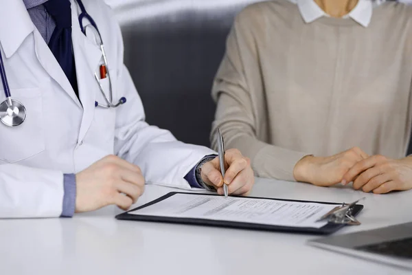 Médico desconhecido e mulher paciente discutindo algo enquanto estava sentado na clínica e usando prancheta. Melhor serviço médico no hospital, medicina, parada pandêmica — Fotografia de Stock