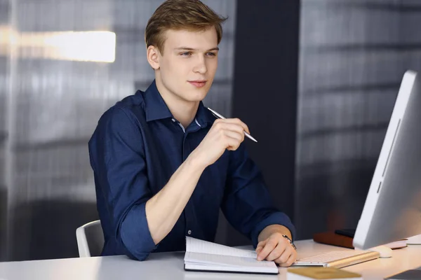 Der junge blonde Geschäftsmann denkt an seinem Arbeitsplatz mit dem Computer über Strategie nach. Start-up-Unternehmen bedeutet, hart zu arbeiten und keine Zeit für Erfolg zu haben — Stockfoto