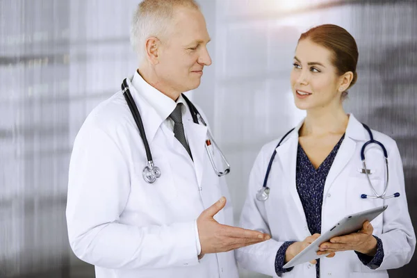 Anziani fiducioso medico e donna-medico discutendo attuale terapia della malattia mentre in piedi in clinica soleggiata. Lavoro di squadra in medicina — Foto Stock