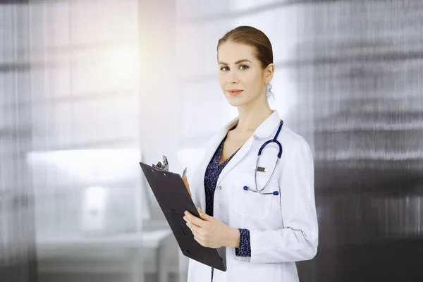 Allegro medico donna in piedi in clinica soleggiata. Ritratto di amichevole sorridente donna-medico. Concetto di medicina — Foto Stock