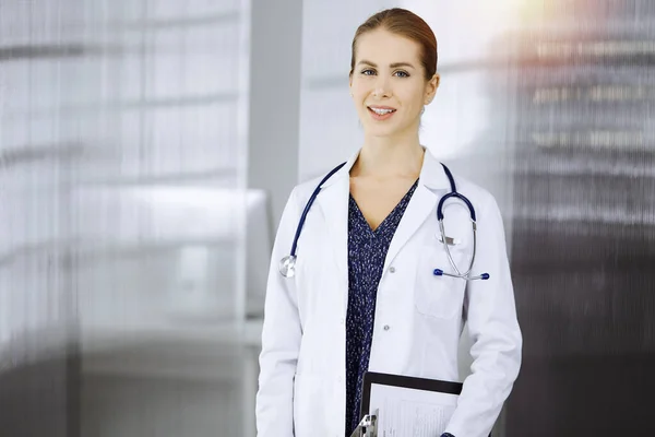 Allegro medico donna in piedi in clinica soleggiata. Ritratto di amichevole sorridente donna-medico. Concetto di medicina — Foto Stock