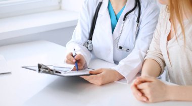 Doktor ve hasta hastanede masa başında otururken bir şey tartışıyorlar, yakın plan. İlaç ve sağlık hizmetleri