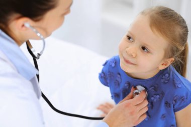 Doktor steteskopla küçük bir kızı muayene ediyor. Her zamanki tıbbi muayenede gülümseyen çocuk hasta. Tıp ve sağlık hizmetleri kavramları