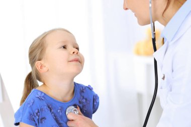Doktor steteskopla küçük bir kızı muayene ediyor. Her zamanki tıbbi muayenede gülümseyen çocuk hasta. Tıp ve sağlık hizmetleri kavramları