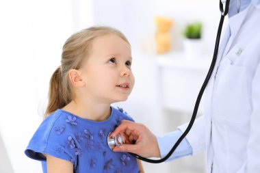 Doktor steteskopla küçük bir kızı muayene ediyor. Her zamanki tıbbi muayenede gülümseyen çocuk hasta. Tıp ve sağlık hizmetleri kavramları